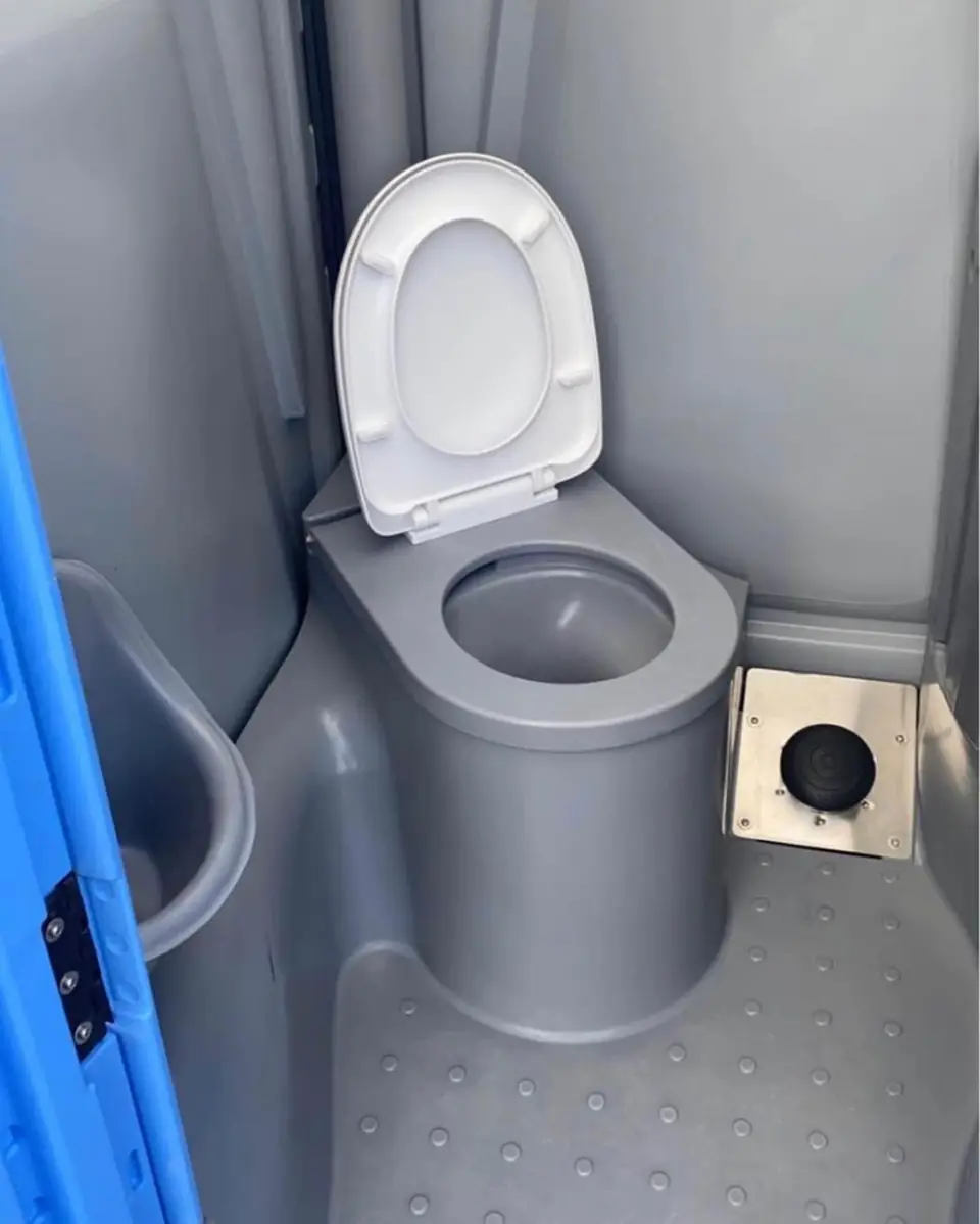 Inside a deluxe flushing porta potty with a white seat and foot pump
