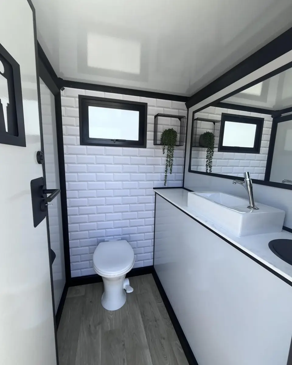 White tiled restroom trailer stall with flushing toilet, vessel sink and mirror