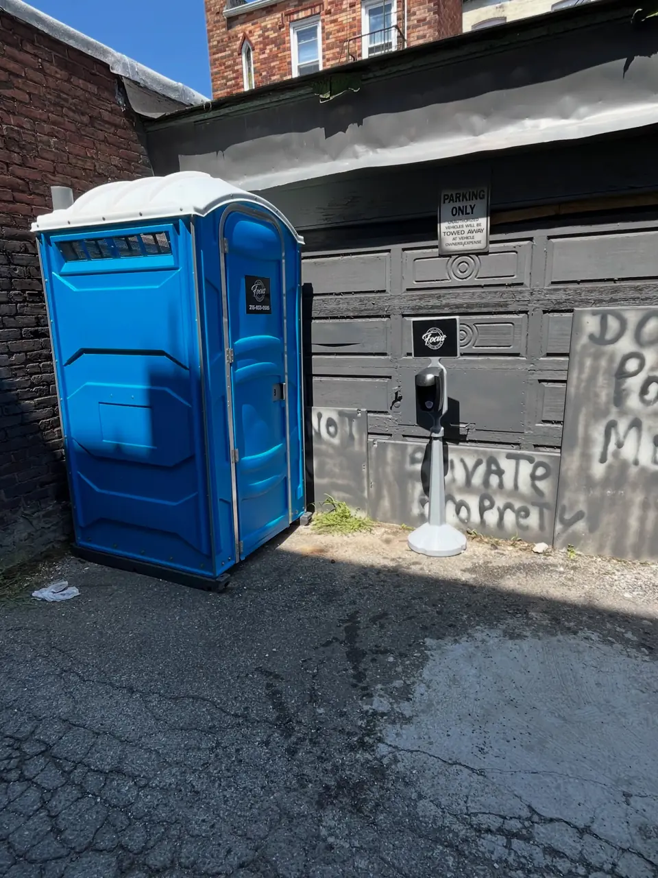 Single blue porta potty placed on a residential driveway next to a garage
